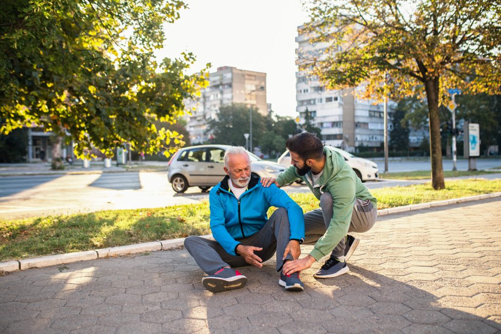 Senior man fallen to the ground with older gentleman helping him back to his feet