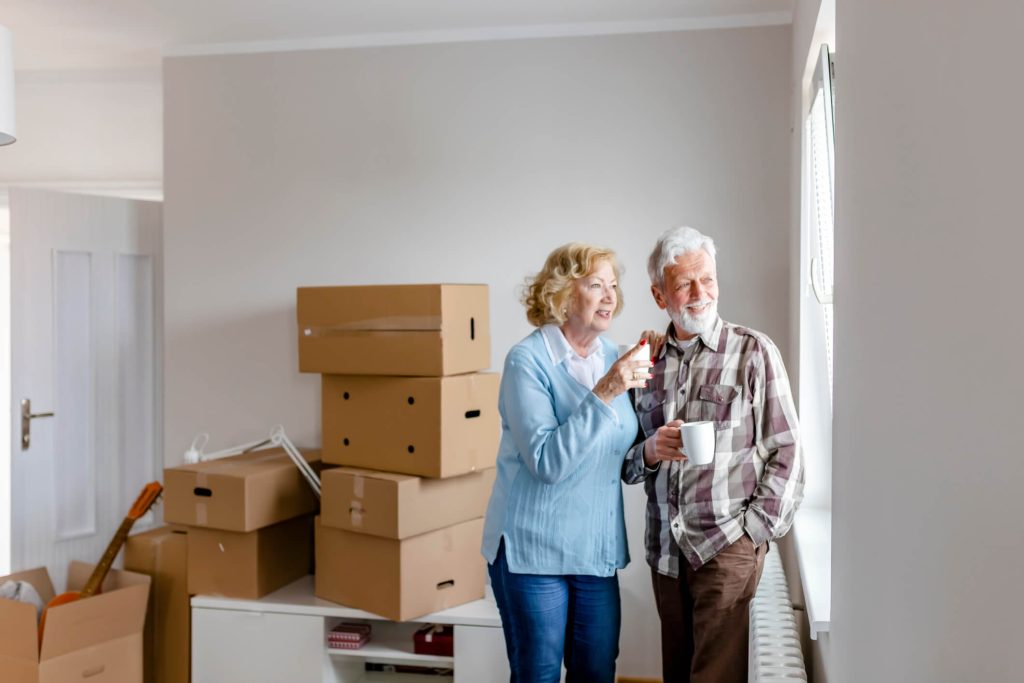 Senior Couple gazing out window with moving boxes behind them