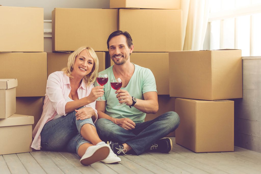 Mature couple sitting in front of boxes holding glasses of wines