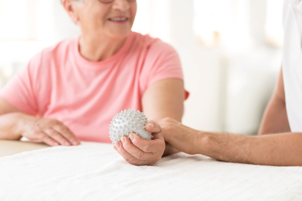 Elderly patient holding grey ball during rehabilitation in the hospital