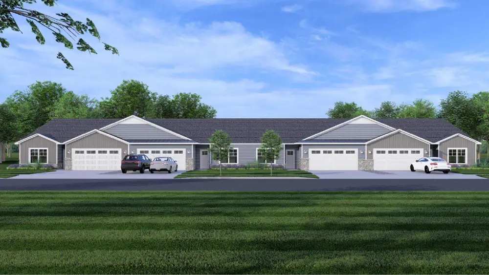 A row of modern duplex homes with garages, set against a clear blue sky and green lawn.